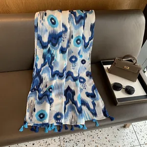 Detail view of blue tie-dye linen scarf with tassels on leather bench with accessories