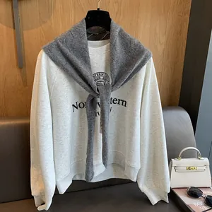 Détail d'un châle en laine grise noué sur un sweat-shirt blanc à logo universitaire chic