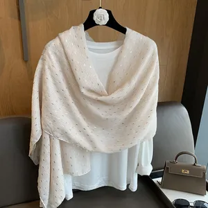 Close-up of soft beige scarf with golden metallic stripes on a minimalist hanger