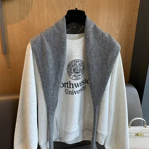 Détail d'un châle en laine grise à losanges porté sur un sweat blanc à imprimé graphique
