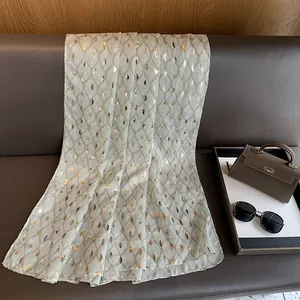 Detail van een dunne katoenen linnen sjaal met gouden bladmotieven en zachte drapering