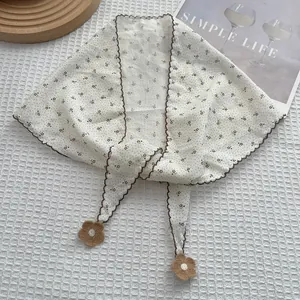 Detail of cream floral neckerchief with wavy brown edges and knitted flower pendants