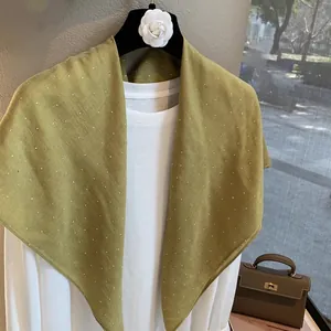 Détail d'un foulard en lin vert moutarde avec strass étincelants sur une chemise blanche