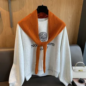 Détail du châle en tricot orange à losanges superposé sur un sweat-shirt gris chiné