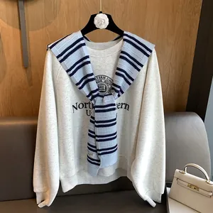 Detail of a blue and white striped knit shawl layered over a beige college sweatshirt
