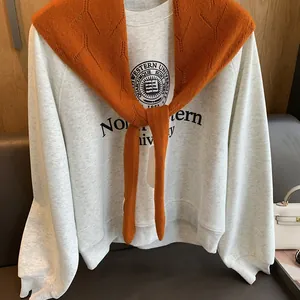 Détail d'un châle en maille caramel sur un sweat-shirt gris à logo universitaire brodé