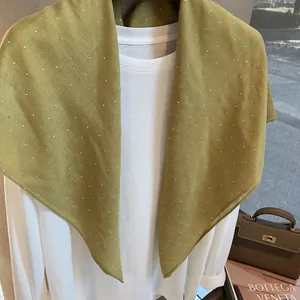 Détail d'une écharpe en lin vert moutarde ornée de strass brillants et texture légère