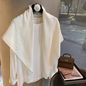 Gros plan d'une écharpe en lin blanc avec des strass brillants portée sur une tenue blanche