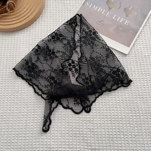Black lace triangle headscarf with floral embroidery and wavy edges in a flat lay view