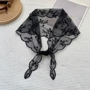 Detail of black floral lace triangle headscarf with scalloped edges on white textured cloth