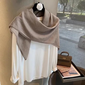 Détail d'un châle en lin marron café avec des strass étincelants sur un haut blanc