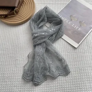 Elegant grey lace scarf with white floral embroidery and scalloped edges on a textured surface