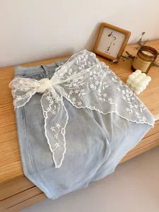 Detail of light blue high-waist jeans featuring delicate white floral lace embroidery belt