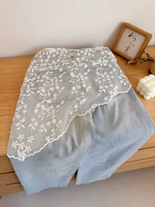 Macro view of light blue denim pants featuring delicate white floral lace and embroidery