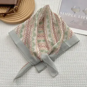 Détail d'un foulard en soie à fleurs vertes avec un sac en cuir marron sur un plateau