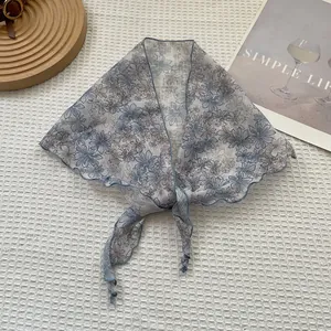 Détail d'un foulard triangle floral gris en tissu semi-transparent et bords ondulés