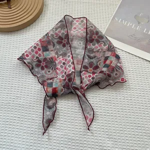 Détail d'un foulard en soie à imprimé floral et bord roulé bordeaux sur tissu texturé