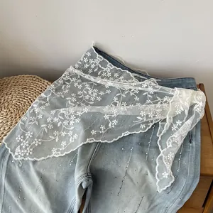 Close-up of white floral lace scarf layered over denim with intricate embroidery details