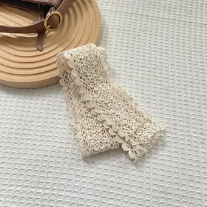 Close-up of cream lace scarf with hollow embroidery flower pattern and wavy edges