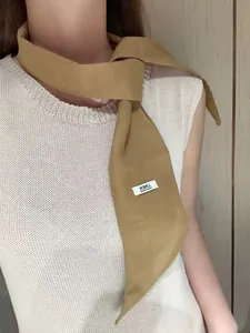 Detail view of mustard linen skinny scarf with handmade label on white knit vest