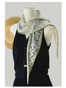 Detailed view of light gray openwork knit scarf with green edges on a mannequin