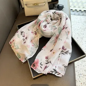 Close-up of lightweight floral scarf with pink blossoms and green leaves on white fabric