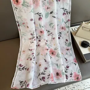 Detail of sheer white scarf with pink floral prints next to a handbag and sunglasses