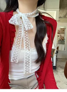 Detailopname van een witte kantensjaal met stippen geknoopt als choker bij een model in rood