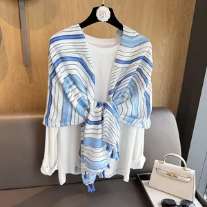 Blue and white striped scarf with tassels layered over a white sweater in a cozy setting