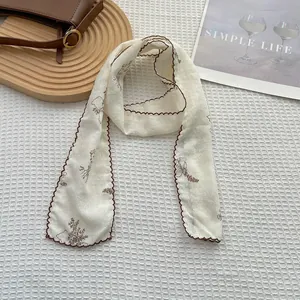Close-up of floral cotton linen skinny scarf with brown scalloped edges on a tray
