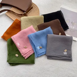 Solid color imitation silk square scarves displayed in multiple colors on a textured surface