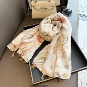 Détail d'une écharpe en soie à motif ethnique avec pompons à côté d'un sac et de lunettes