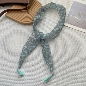 Dettaglio di una sciarpa sottile floreale azzurra con nappe su sfondo a trama di griglia