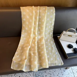 Close-up of yellow silk scarf with white polka dots on a leather surface with accessories