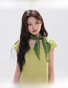 Detail of green silk scarf tied on yellow top with oval metal buckle accessory
