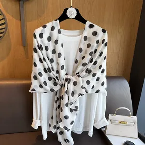 Classic French style white silk scarf with black polka dots draped over a white blouse