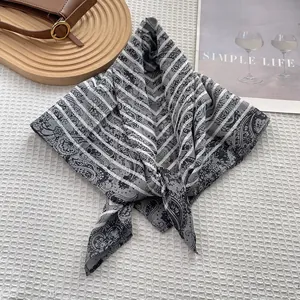 Detalle de bufanda de seda con estampado paisley, bandeja de madera y libro minimalista