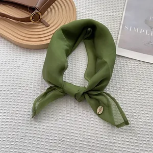 Detailed close-up of retro green silk scarf with delicate stitching and golden metal charm