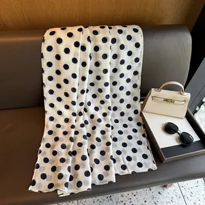 French vintage polka dot silk scarf draped on a leather sofa with chic accessories