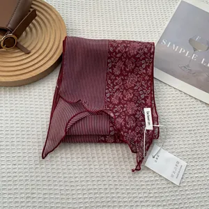Detail view of burgundy striped floral silk scarf with branded tag on white textured background