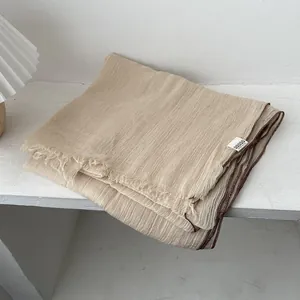 Detalle de bufanda de lino beige con textura arrugada, flecos y un borde marrón
