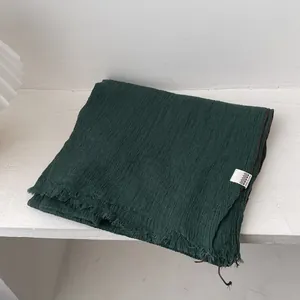 Detalle de bufanda de lino verde oscuro con textura plisada y bordes de flecos finos