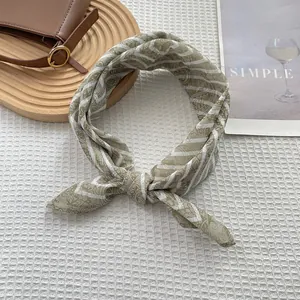 Detalle de un pañuelo de seda verde y blanco con motivos paisley y rayas en tela blanca