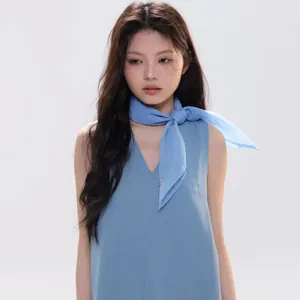 Close-up of a light blue silk-like square scarf tied in a bow on a model's neck