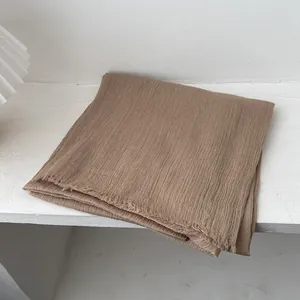 Vista detallada de bufanda de lino marrón con textura arrugada y bordes deshilachados