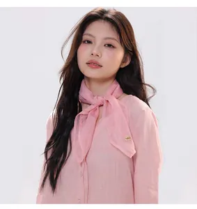 Detail of pink silk scarf with gold logo buckle worn with a linen shirt on a model