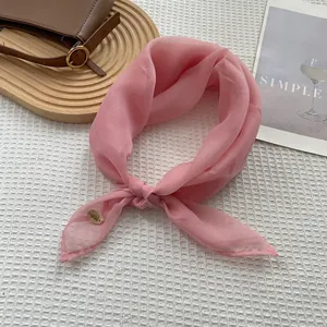 Detailed view of pink chiffon scarf with gold logo tag on a waffle texture background