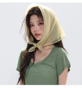Detail of a sheer light yellow silk headscarf paired with a green knit V-neck t-shirt