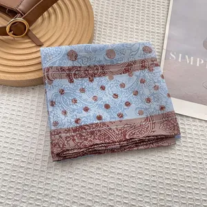 Pale blue and brown paisley polka dot silk scarf displayed on a white textured background