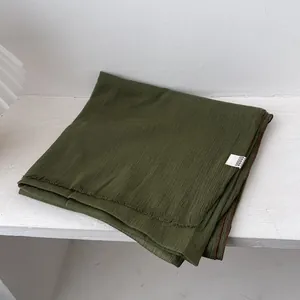 Detalle de bufanda de lino verde oscuro con textura plisada y bordes con flecos finos